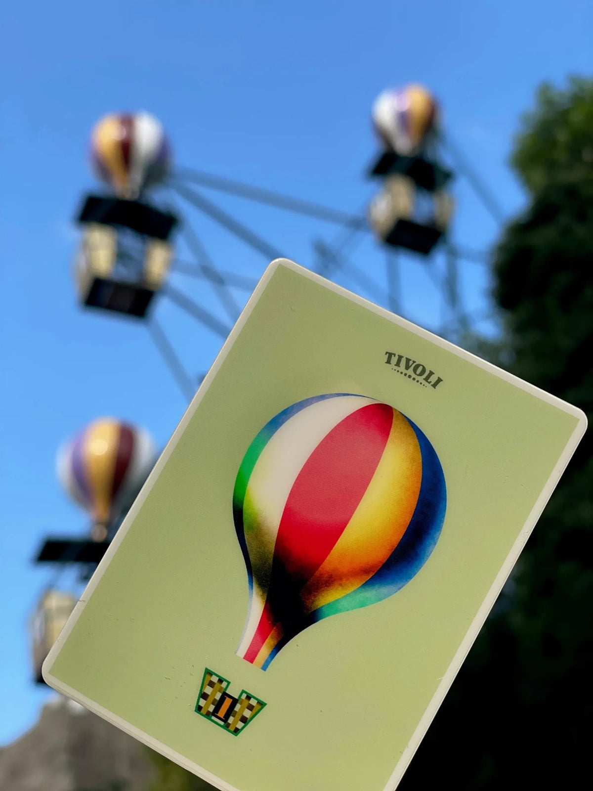 Ballongynge magnet med farverigt motiv af Mads Berg, fotograferet foran Tivolis ikoniske Ballongynge med luftballoner i baggrunden.