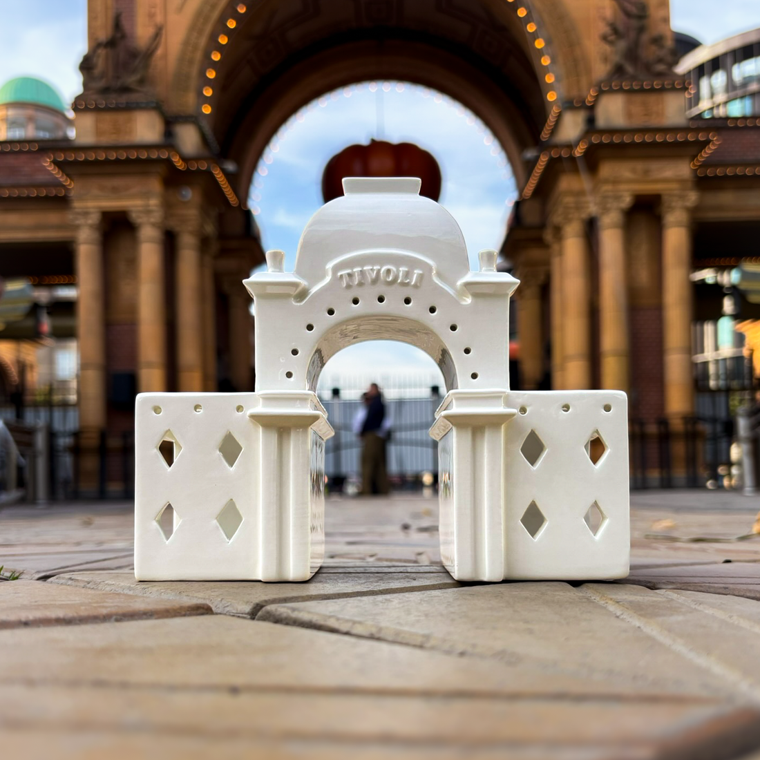 Tivoli x Kähler Urbania lyshus formet som Tivolis ikoniske Hovedindgang. Det hvide keramiske lyshus har buet portåbning, kuppelformet tag, udskårne vinduer og fine arkitektoniske detaljer inspireret af den historiske indgang til Tivoli.