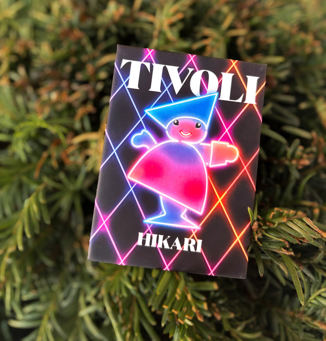 Little Tivoli Hikari Pjerrot-magnet med neoninspireret design, lysende farver og Tivolis ikoniske Pjerrot på mørk baggrund med farverige lysmønstre.