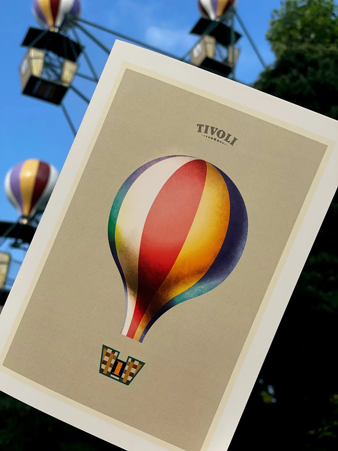 Foldekort med Mads Berg illustration af Tivolis ikoniske Ballongynge, fotograferet foran forlystelsen med farverige luftballoner i baggrunden.