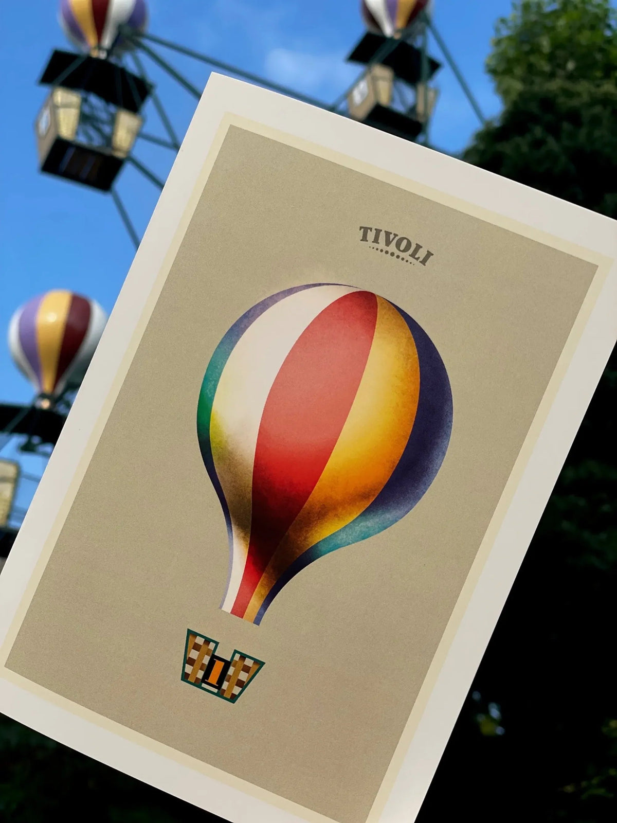 Foldekort med Mads Berg illustration af Tivolis ikoniske Ballongynge, fotograferet foran forlystelsen med farverige luftballoner i baggrunden.