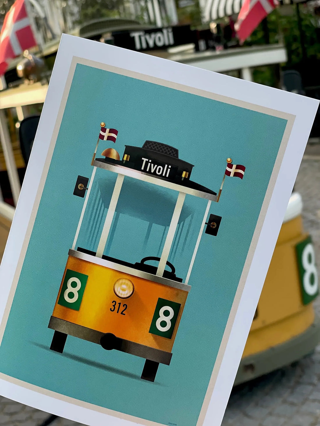 Foldekort med Mads Bergs illustration af Tivolis ikoniske Linie 8-sporvogn, fotograferet foran forlystelsen i Tivoli.