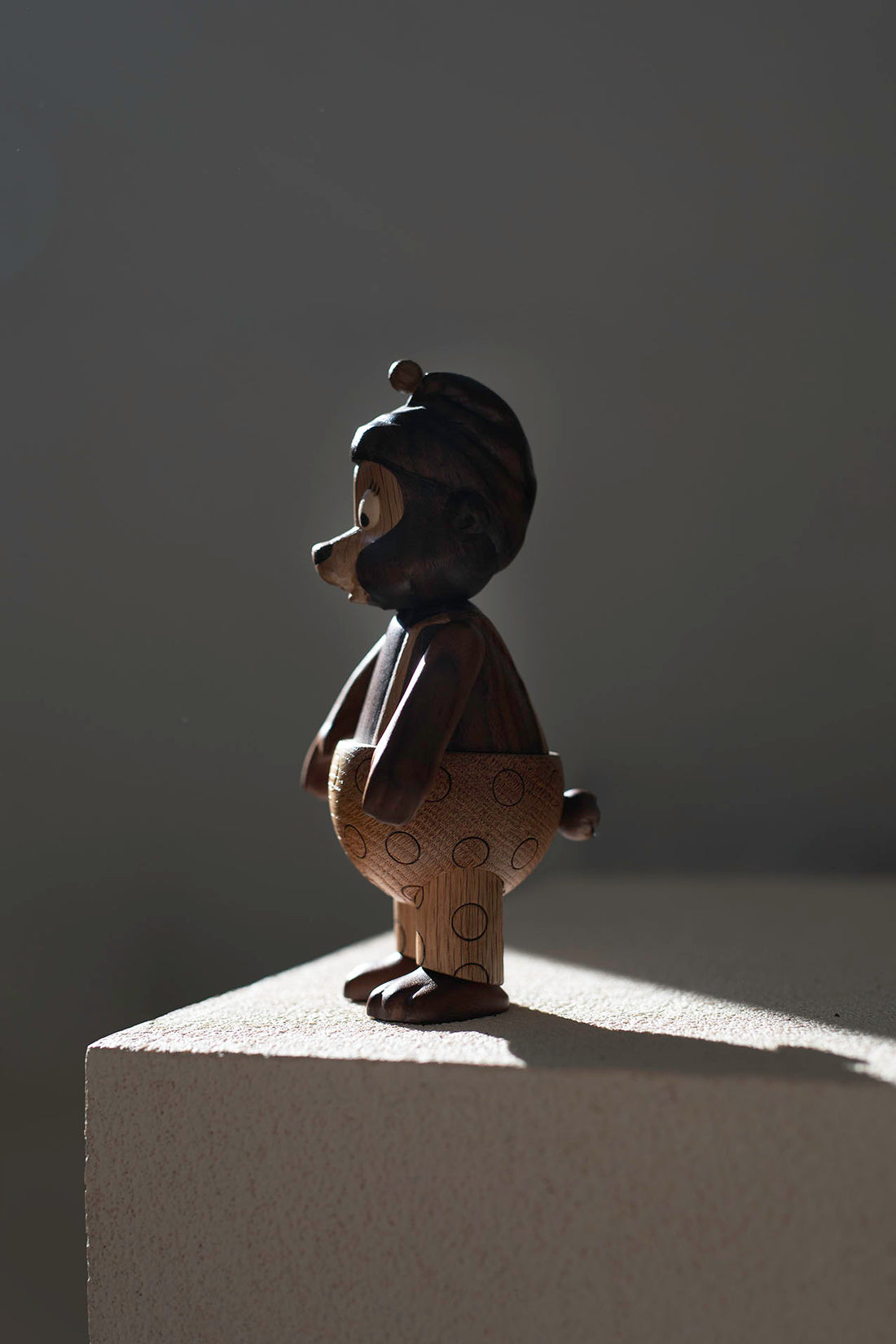 Rasmus Klump-maskot holder en træfigur af Rasmus Klump frem. Figuren er fremstillet i FSC-certificeret egetræ og valnød og vises i Tivoli-miljø.