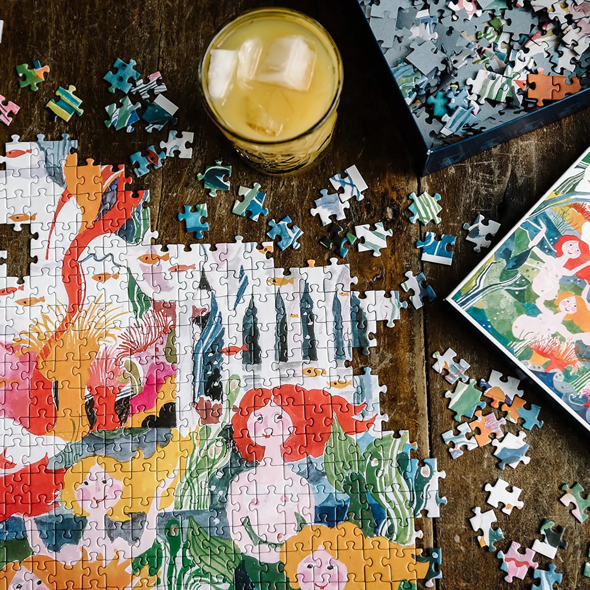 The Little Mermaid 1000-piece jigsaw puzzle by Hans Christian Andersen being assembled on a wooden table, featuring vibrant mermaids, sea life and underwater scenery. Exclusive to Little Tivoli.