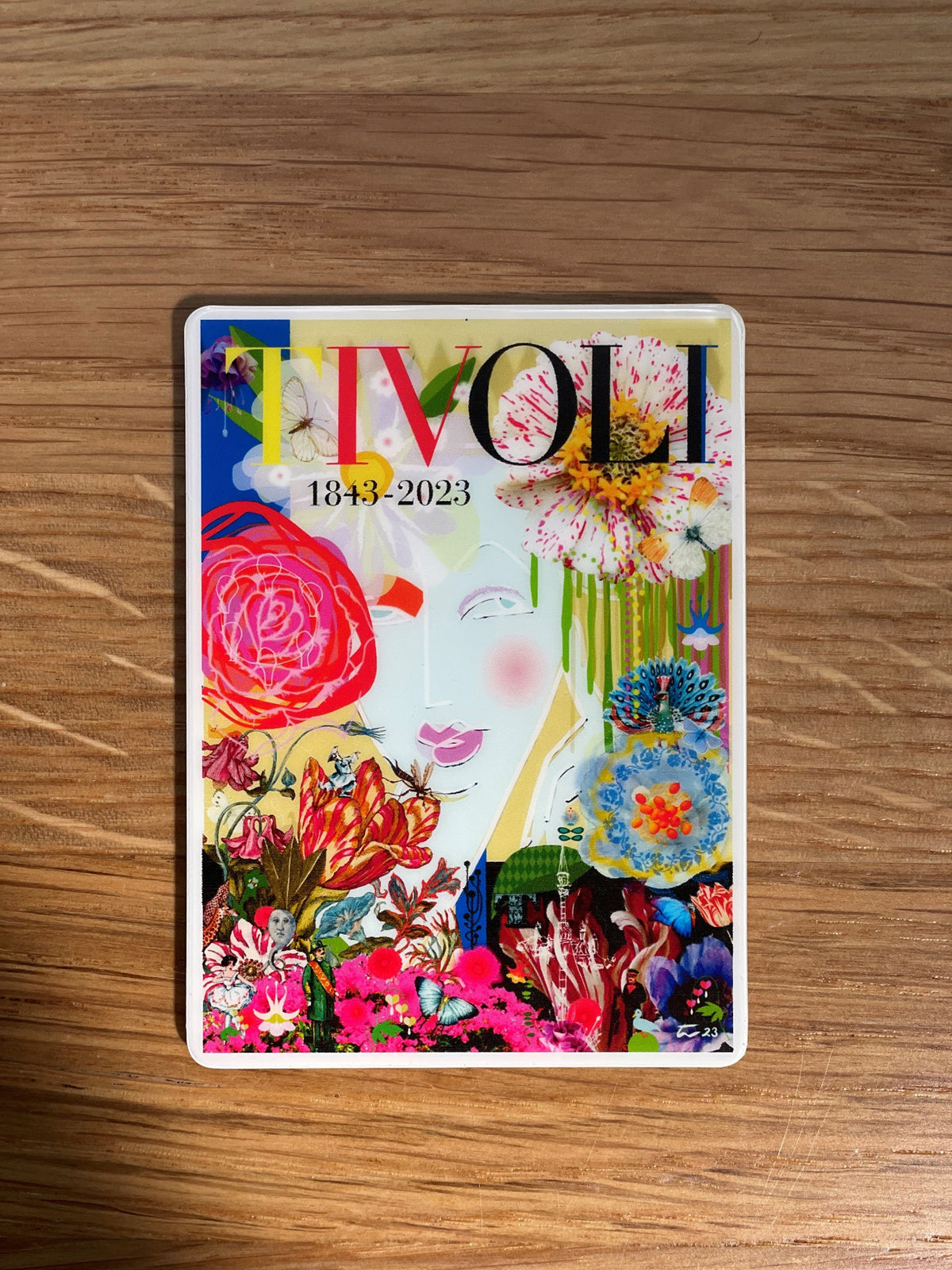Tivoli 180 års jubilæumsmagnet med farverigt motiv af Thomas Winkler, fotograferet på træbord med detaljer inspireret af Tivolis blomster, haver og ikoniske oplevelser.