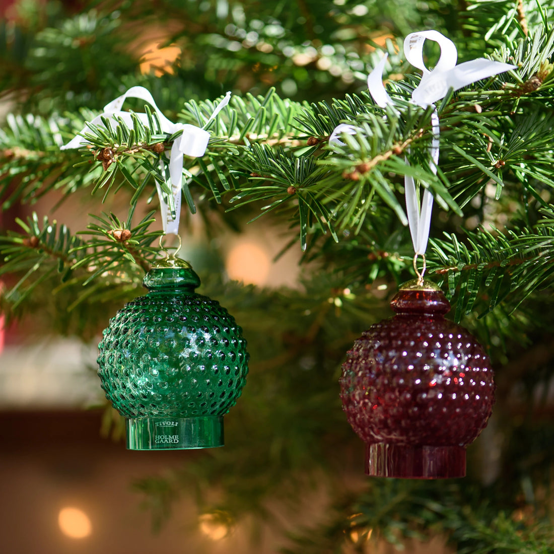 Tivoli x Holmegaard Kuppel juleophæng i rubinrødt glas med dekorativ boblestruktur inspireret af den ikoniske Tivoli Kuppel. Juleophænget har hvidt ophængsbånd og indgraveret Tivoli x Holmegaard-logo på foden.
