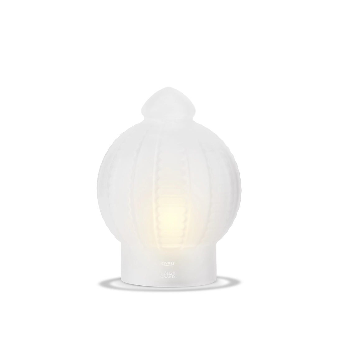 Tivoli x Holmegaard glaslampe i hvidt opalglas med dekorative lodrette relieffer og blødt lys, der stråler gennem glasset. Lampen har en karakteristisk kuppelformet top og fod med diskret Tivoli x Holmegaard-logo.