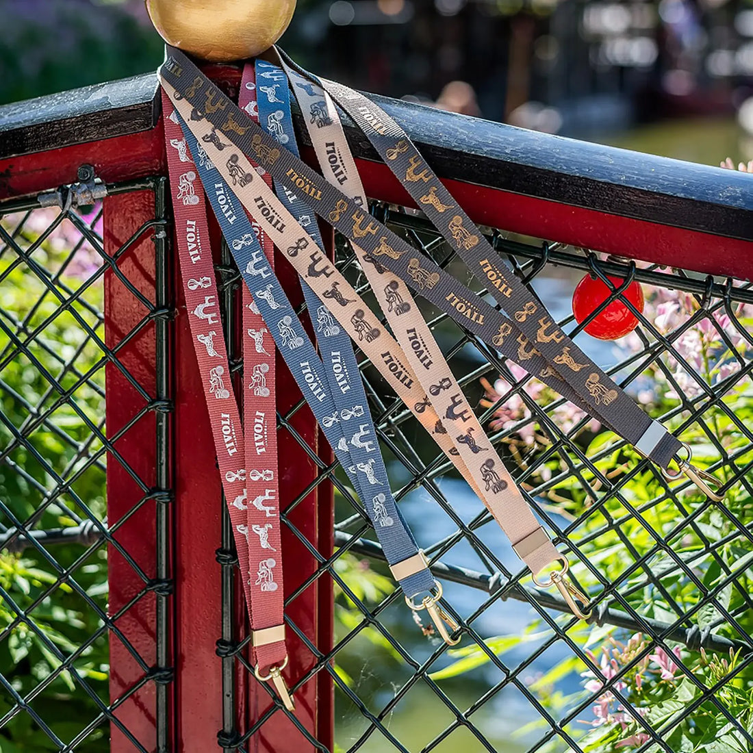 Tivoli nøglesnor i genanvendt plast med ikoniske Tivoli-motiver og guldfarvet karabinhage båret om halsen med nøgler fastgjort.