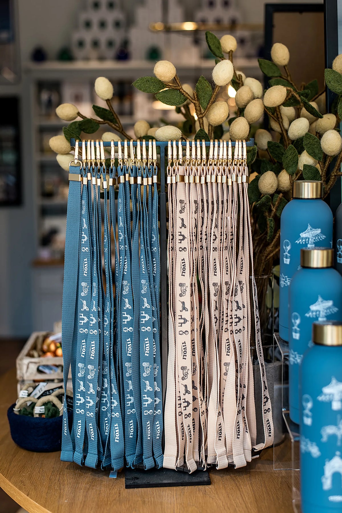 Tivoli nøglesnore i genanvendt plast udstillet på et bord i Tivoli-butikken. Nøglesnorene ses i blå, beige og brun med ikoniske Tivoli-motiver og guldfarvede detaljer.