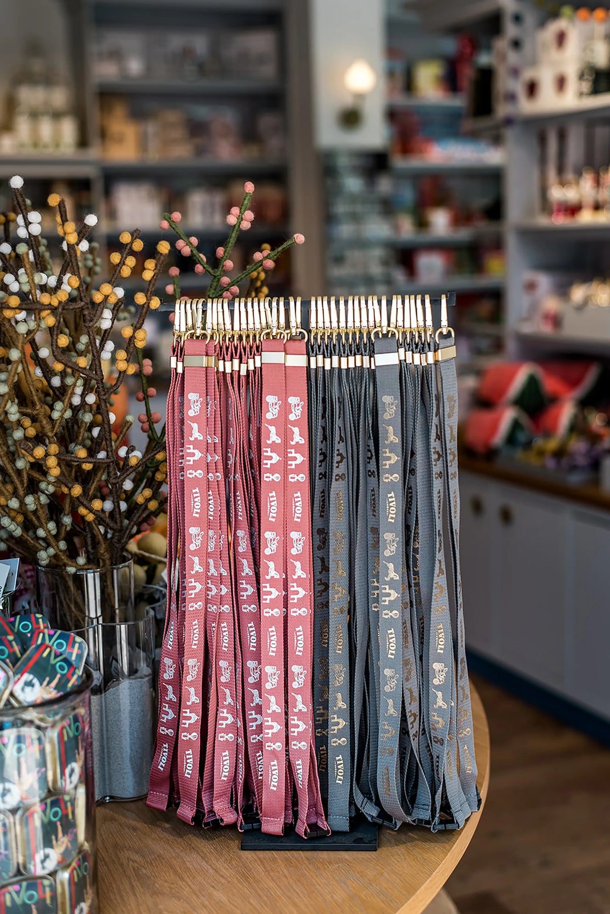 Tivoli nøglesnore i flere farver udstillet på et display i en Tivoli-butik. Nøglesnorene er dekoreret med ikoniske Tivoli-motiver og har guldfarvede karabinhager.