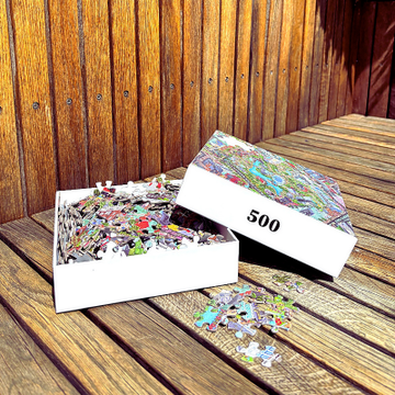 Colourful 500-piece Tivoli Gardens puzzle by IC4, featuring detailed illustrations of Copenhagen’s iconic amusement park, puzzle box and loose pieces on a wooden surface.