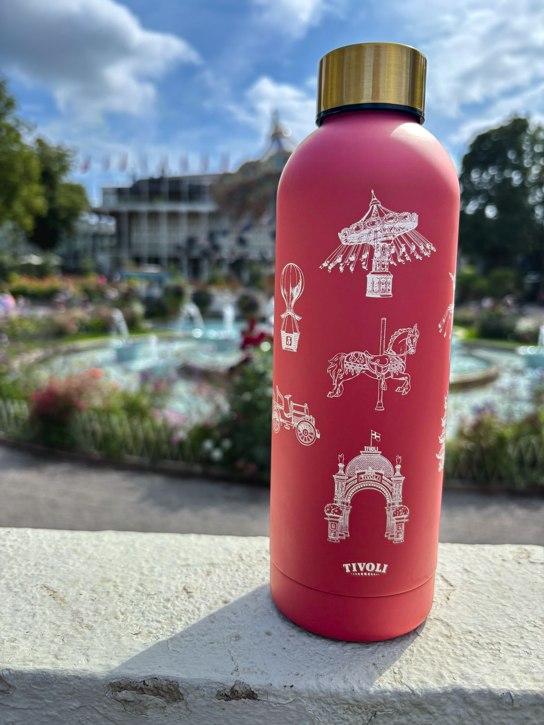 Rosa Tivoli termoflaske med guldfarvet skruelåg og detaljerede hvide illustrationer af Tivolis ikoniske bygninger og forlystelser, herunder Hovedindgangen, Karussellen og Ballongyngen.