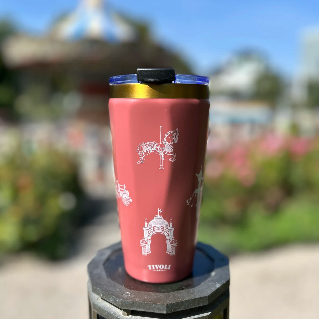 Rosa Tivoli To-Go termokrus med guldfarvet kant og hvide illustrationer af Tivolis ikoniske bygninger og forlystelser, herunder Hovedindgangen, Karussellen og Ballongyngen.
